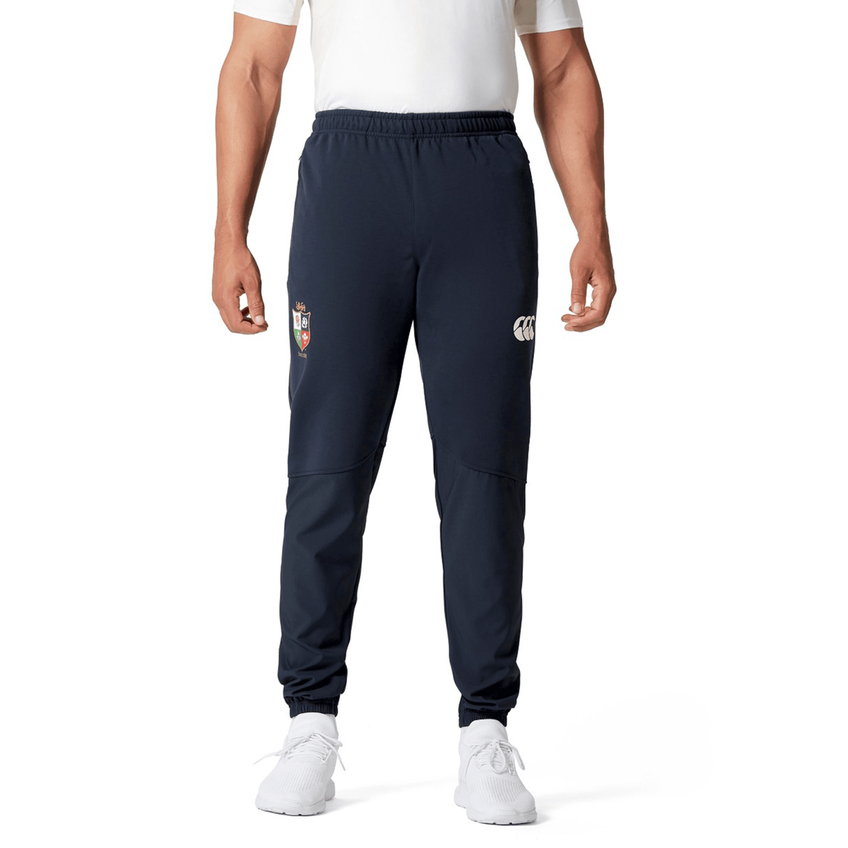 A person wearing a white shirt, British &amp; Irish Lions 25 Training Pants by Canterbury in navy with patches, and white sneakers.