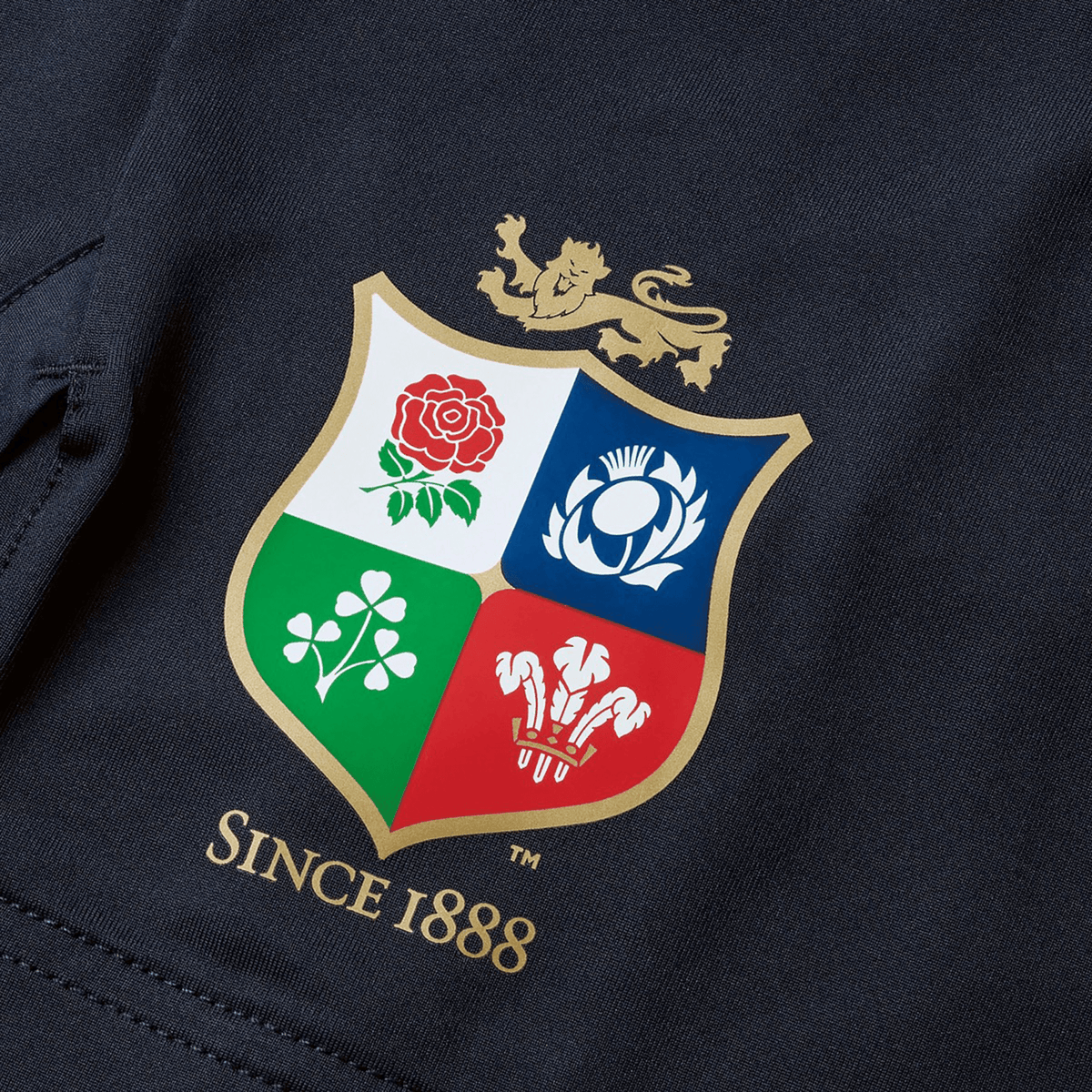 A detailed view of a crest displaying a lion above four quadrants adorned with a rose, thistle, shamrock, and feathers. Below the emblem is the inscription "Since 1888," honoring the rich heritage of the British &amp; Irish Lions. This tribute is featured on the British &amp; Irish Lions 2025 Training Short by Canterbury.