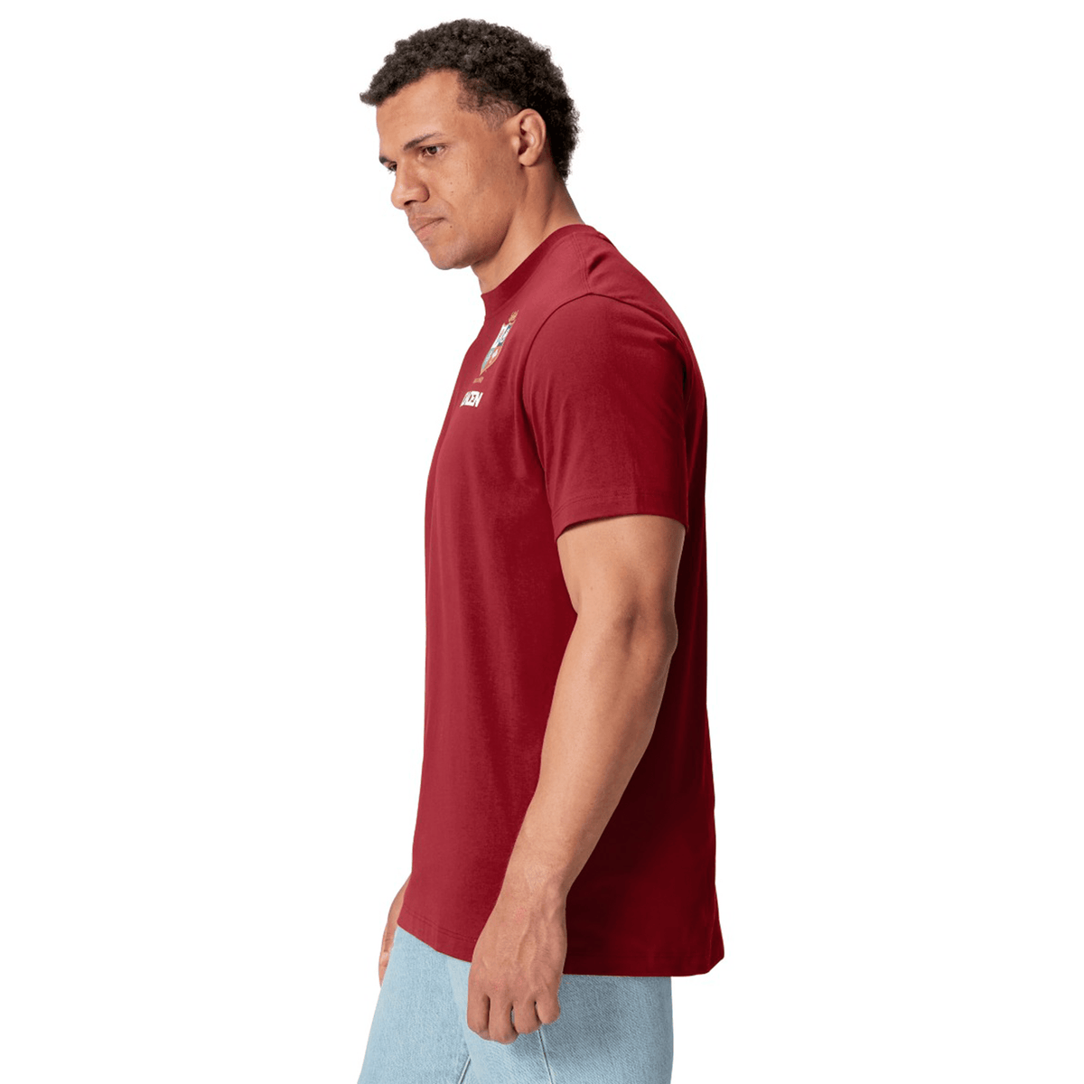 A man wearing the British &amp; Irish Lions 2025 Cotton Jersey Tee by Canterbury and light blue jeans stands against a white background, facing slightly left. He has the confident stance of a rugby supporter, reminiscent of fans cheering for the British &amp; Irish Lions.
