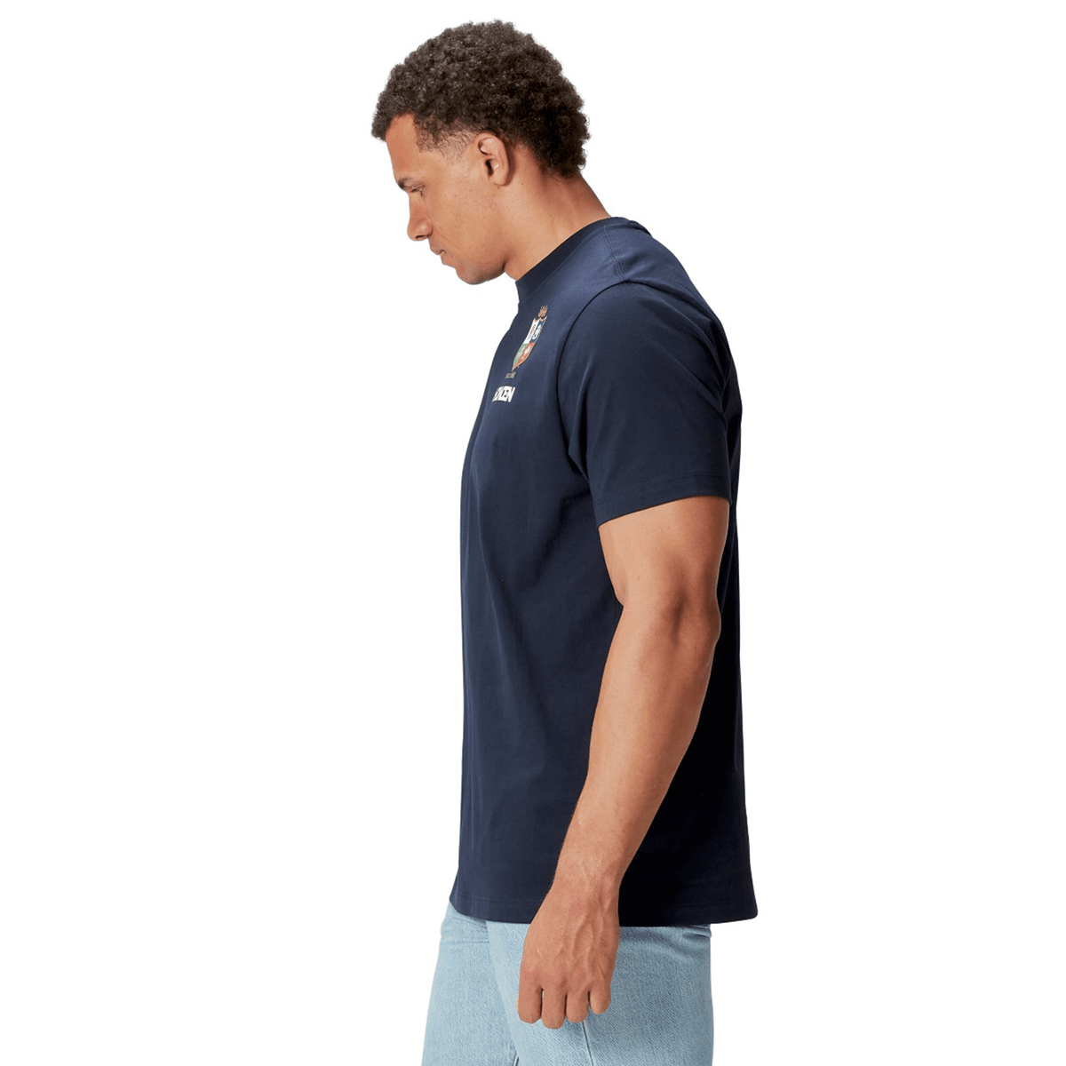 A model wearing the British &amp; Irish Lions 2025 Cotton Jersey Tee by Canterbury and light blue jeans, crafted from organic cotton, stands in profile against a white background.