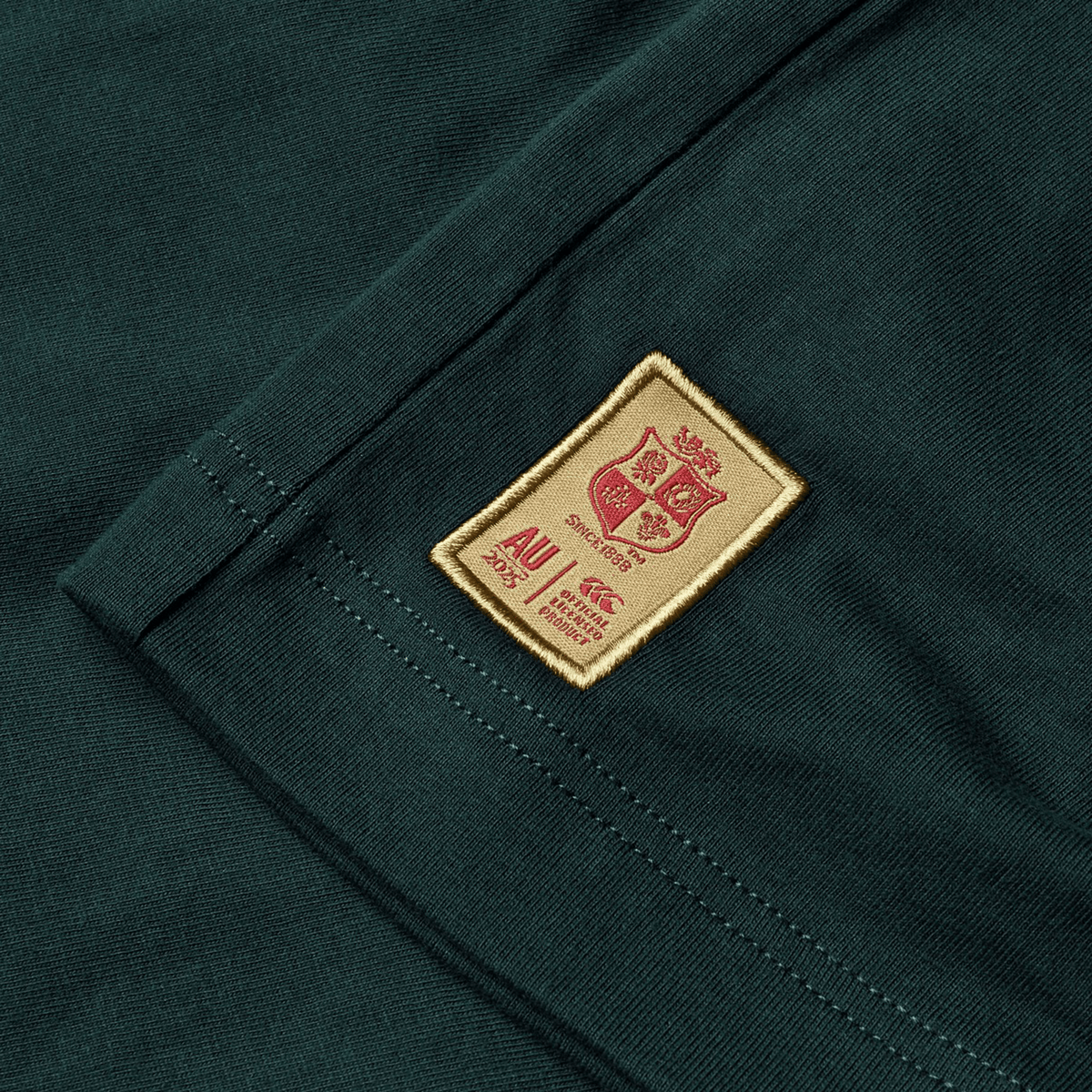 The British &amp; Irish Lions 2025 Cotton Jersey Tee by Canterbury is crafted from organic cotton in a striking green with a distinctive brown patch, showcasing a crest and text that make it ideal for any rugby supporter.