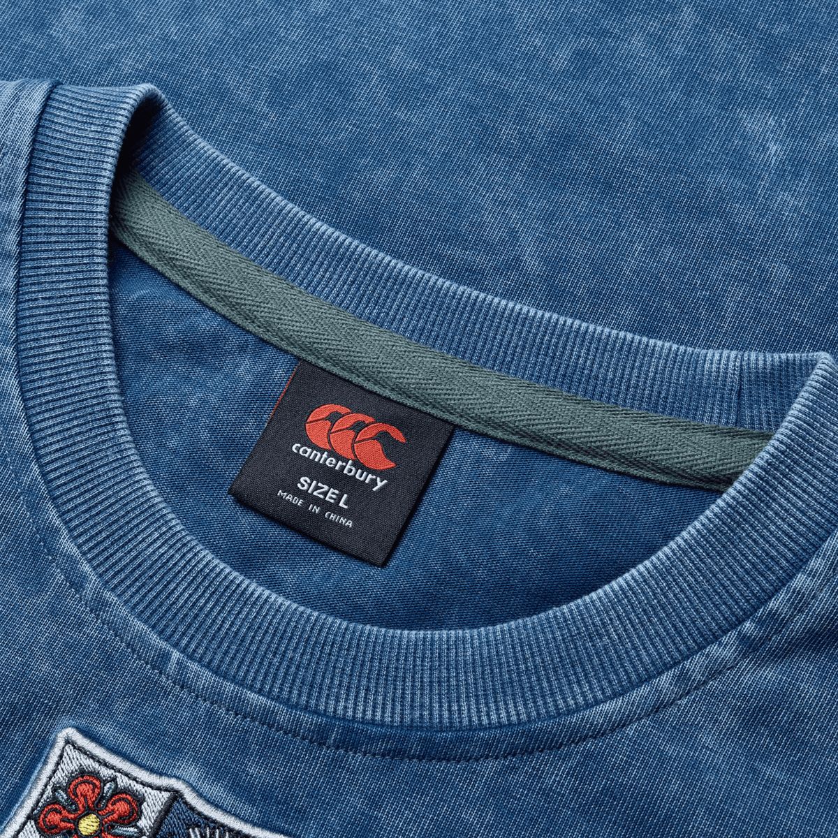 Close-up of a blue British &amp; Irish Lions 25 Heritage Tee by Canterbury featuring a visible collar and tag that reads, &quot;Canterbury SIZE L Made in China.