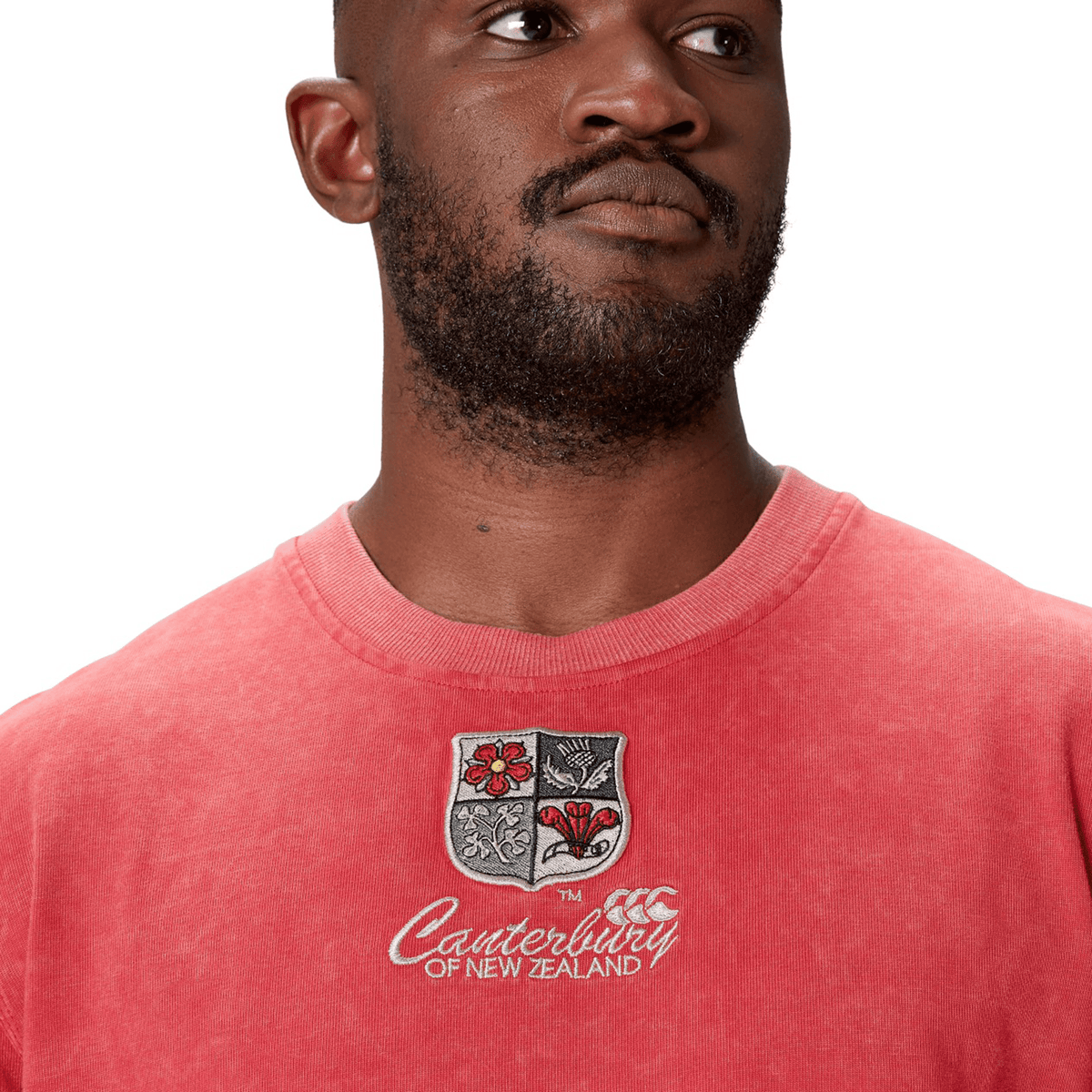 A person wearing a red British &amp; Irish Lions 25 Heritage Tee by Canterbury, crafted from organic cotton, featuring an embroidered crest on the chest.