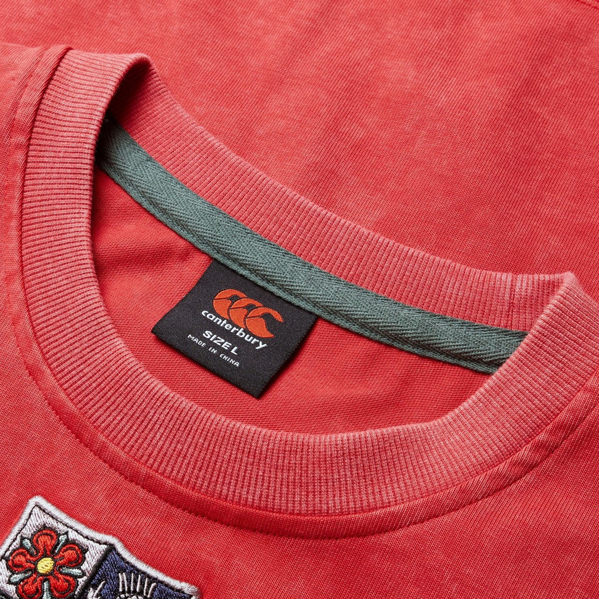 Close-up of a British &amp; Irish Lions 25 Heritage Tee by Canterbury in red, highlighting the visible Canterbury label inside the collar. A small, colorful patch is artfully sewn on the fabric, evoking the classic style beloved by fans of the British &amp; Irish Lions.