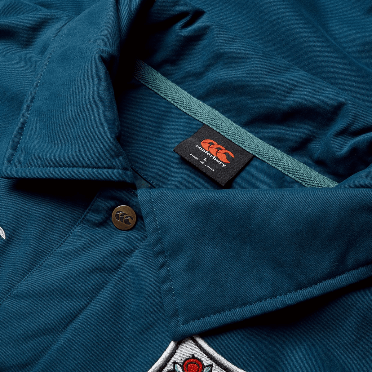 Close-up of the collar of a Canterbury British &amp; Irish Lions 2025 Heritage Quilted Jacket, detailed with a button, tag, and part of an embroidered design that reflects the classic style associated with British &amp; Irish Lions attire.