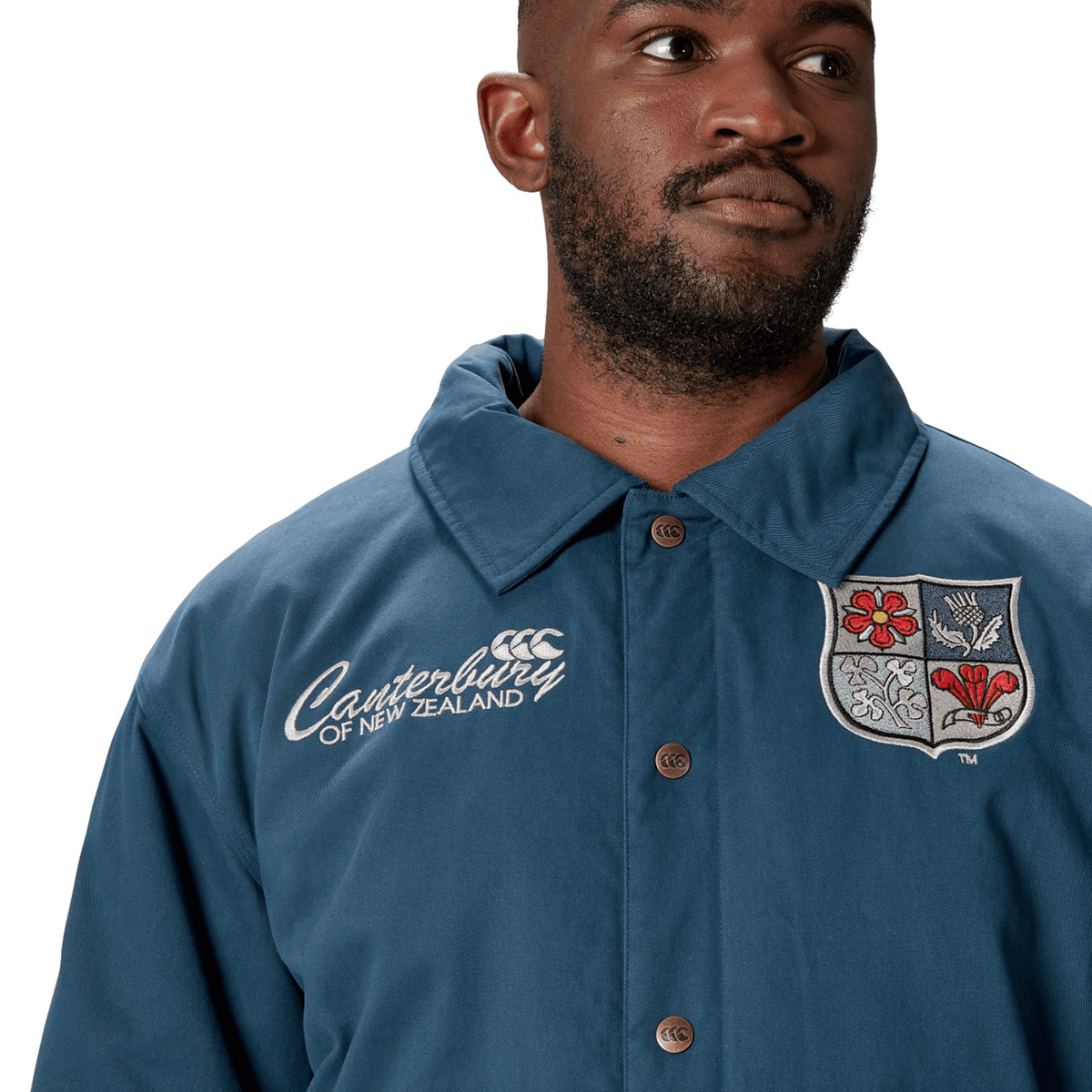 A man wears the British &amp; Irish Lions 2025 Heritage Quilted Jacket by Canterbury, showcasing a crest and embroidered logo in a blue design that evokes the classic style linked with the esteemed British &amp; Irish Lions.