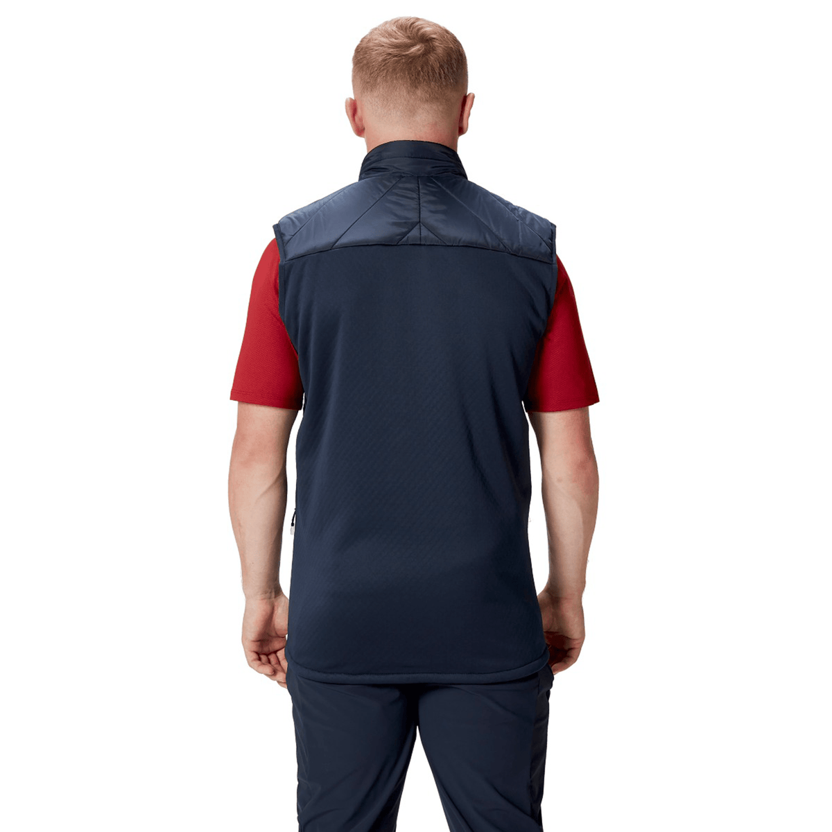 A person with short blonde hair is standing, facing away, wearing a British &amp; Irish Lions 2025 Microlight Gilet by Canterbury made from recycled polyester over a red short-sleeve shirt and navy pants.