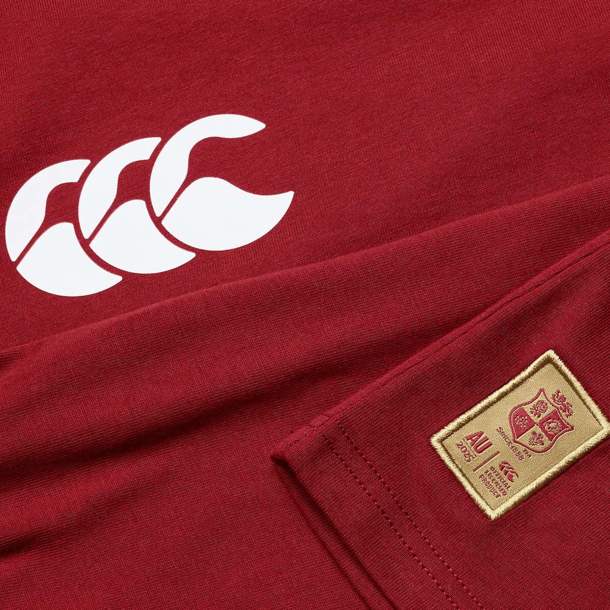 A close-up of the Women's British &amp; Irish Lions 25 Cotton Jersey Tee by Canterbury showcases its red design made from organic cotton, highlighted by a white logo and a beige patch adorned with the British &amp; Irish Lions crest and text.