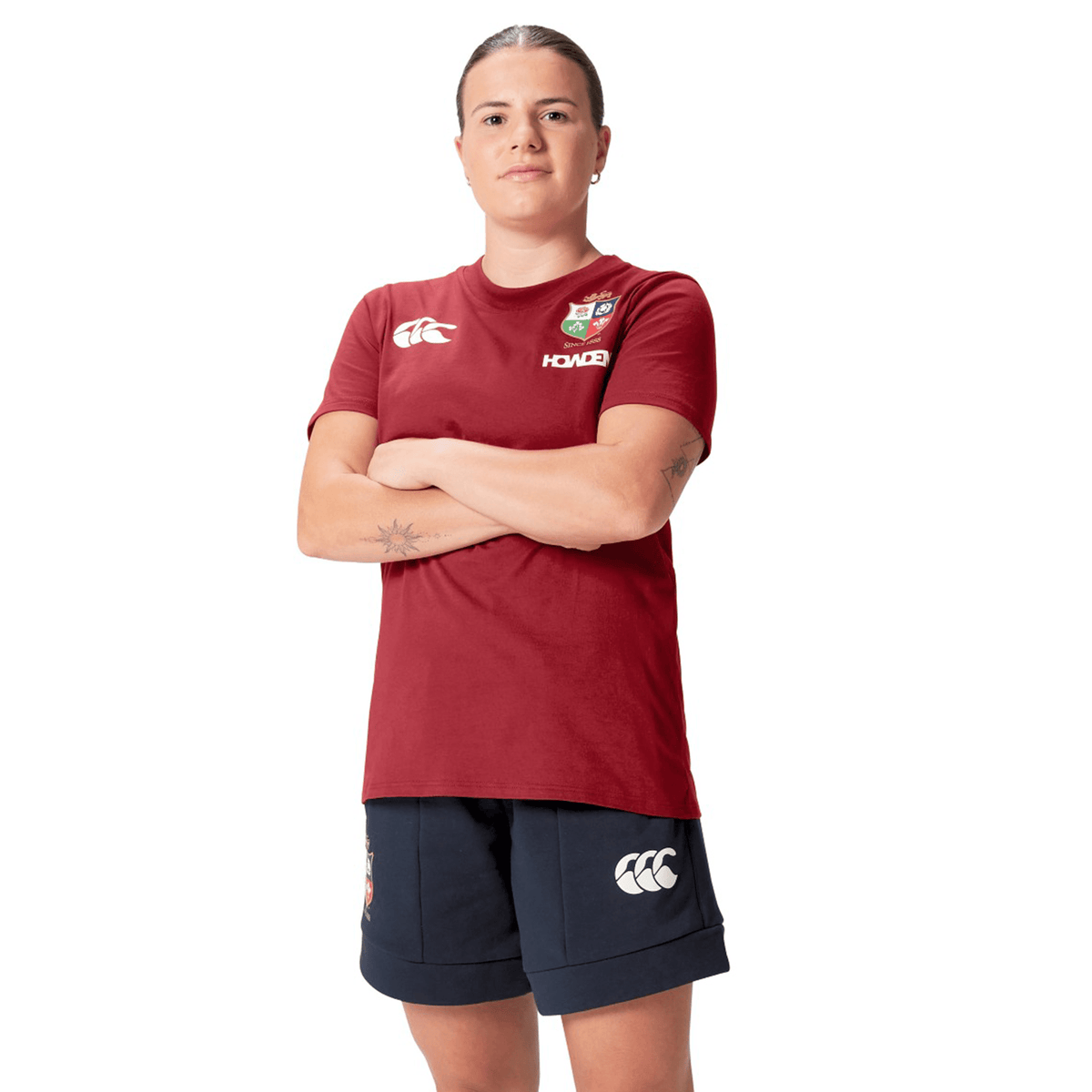 A rugby supporter in the Women's British &amp; Irish Lions 25 Cotton Jersey Tee by Canterbury, paired with navy shorts, stands with arms crossed. The outfit is made from organic cotton.