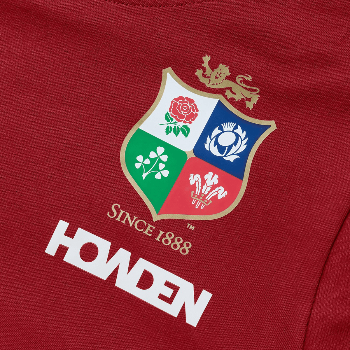 Introducing the Women's British &amp; Irish Lions 25 Cotton Jersey Tee by Canterbury, a red shirt made from organic cotton. It features a vibrant multi-colored sports emblem adorned with symbols of a rose, thistle, shamrock, and dragon. Perfect for rugby enthusiasts, this tee proudly displays the text "SINCE 1888" and "HOWDEN," reflecting the spirit of the British &amp; Irish Lions.