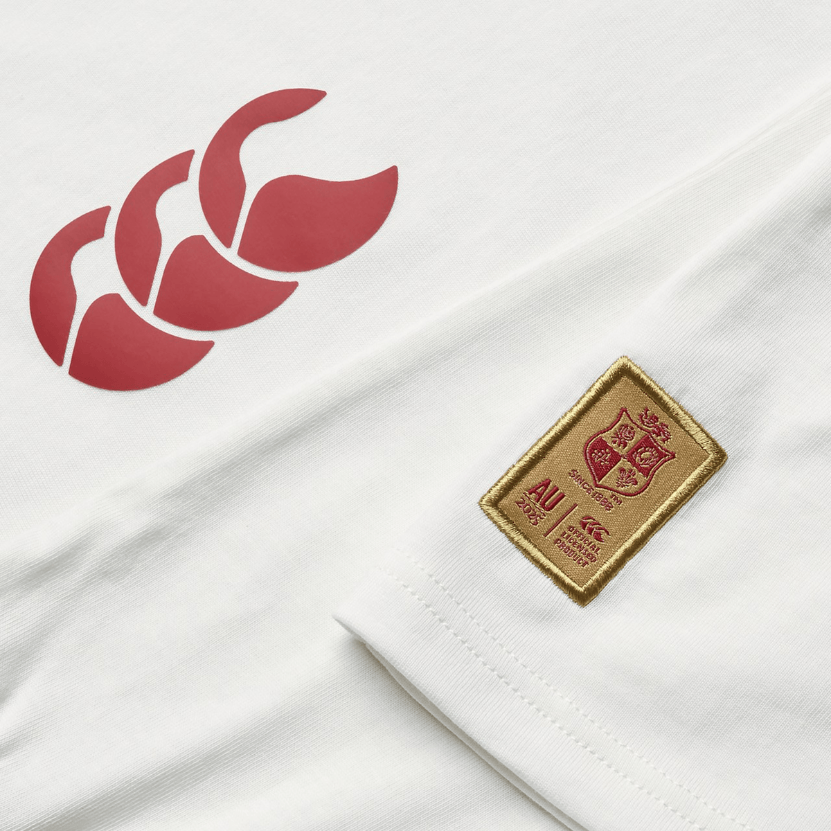 The Women's British &amp; Irish Lions 25 Cotton Jersey Tee by Canterbury, made from organic cotton, showcases a red triple-leaf logo on the left and an embroidered golden shield patch on the right bearing a coat of arms and the letters "AU".