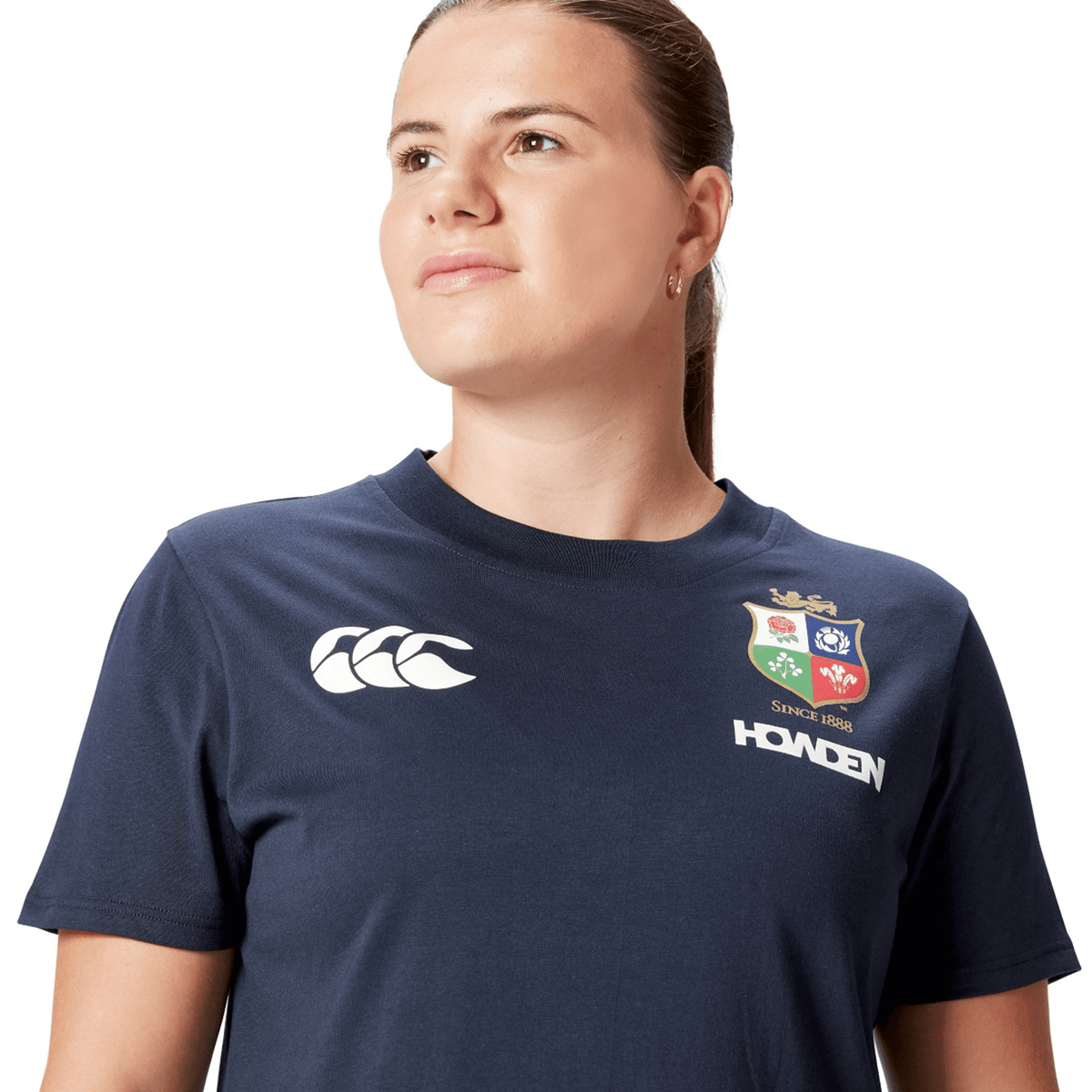 A rugby supporter in a Women's British &amp; Irish Lions 25 Cotton Jersey Tee by Canterbury, featuring navy with sports logos, glances to the side against the white background.
