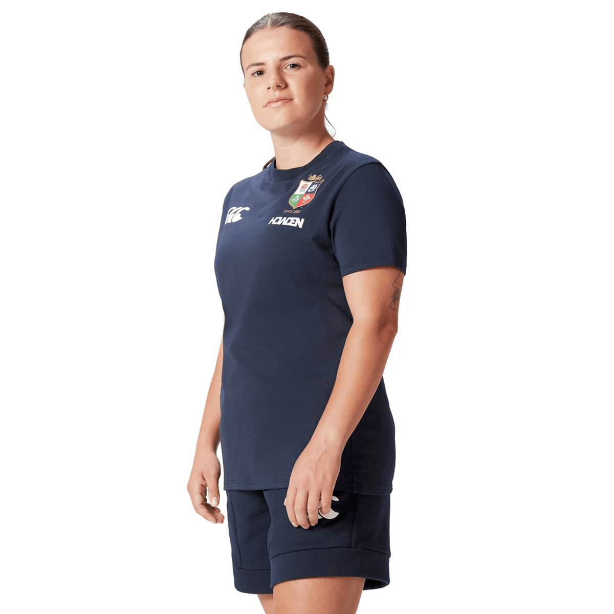 A rugby fan in a navy blue *Women's British &amp; Irish Lions 25 Cotton Jersey Tee by Canterbury* stands against a white background, looking confidently at the camera.