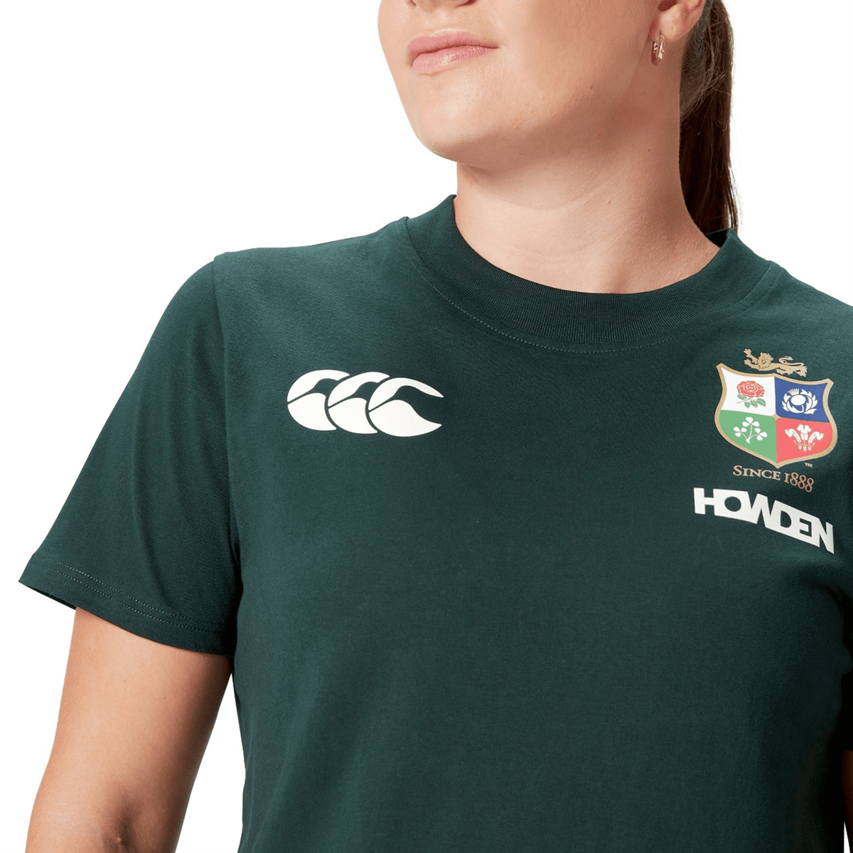 A person proudly wears a Women's British &amp; Irish Lions 25 Cotton Jersey Tee by Canterbury in green, made from organic cotton, featuring a logo and the text "Howden" and "Since 1888.