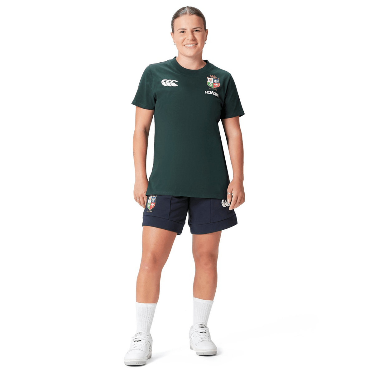 A person dressed in the Women's British &amp; Irish Lions 25 Cotton Jersey Tee by Canterbury, complemented by navy shorts, white socks, and sneakers, stands against a plain white background.
