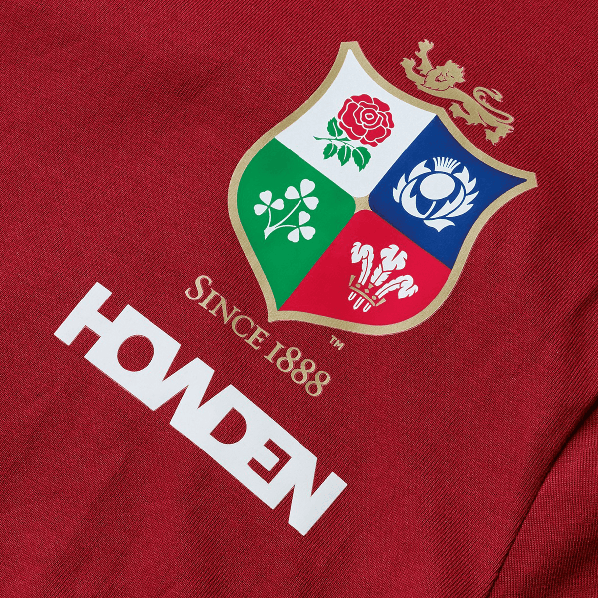 The Youth British &amp; Irish Lions 2025 Cotton Jersey Tee by Canterbury features red fabric with a crest bearing a rose, thistle, shamrock, and feathers, along with &quot;Since 1888&quot; above &quot;HOWDEN.&quot; An ideal tribute for the passionate rugby supporter.