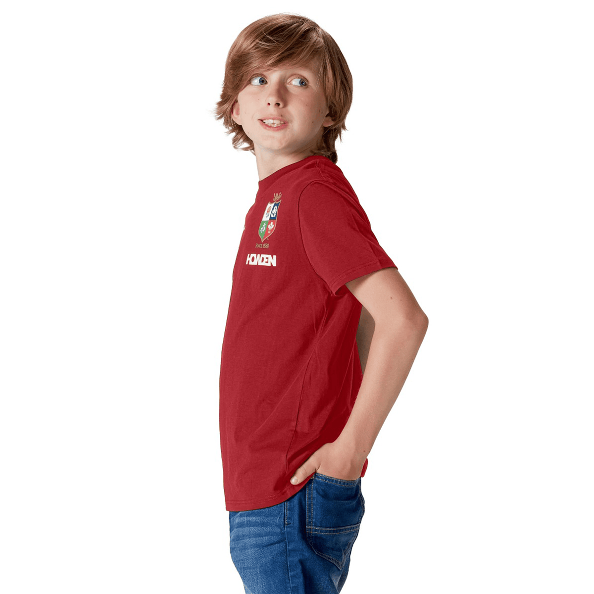 A young rugby fan wearing the Youth British &amp; Irish Lions 2025 Cotton Jersey Tee by Canterbury stands casually with hands in his jeans pockets, glancing to the side against a white backdrop.