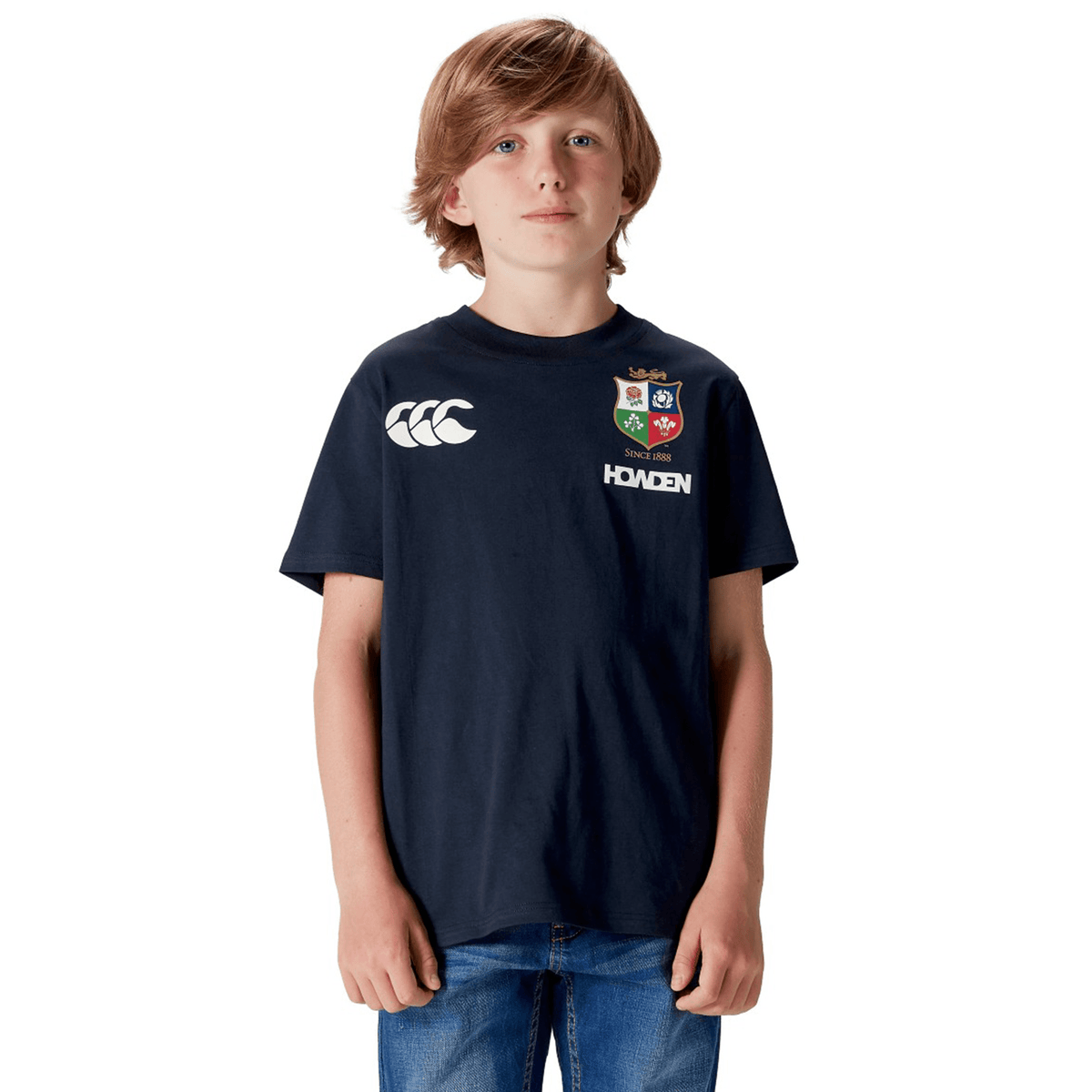 A boy in a Canterbury Youth British &amp; Irish Lions 2025 Cotton Jersey Tee and blue jeans, against a white background, exudes true rugby supporter spirit.