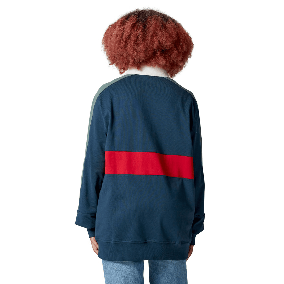 A person with curly hair, wearing the classic navy British &amp; Irish Lions 2025 Heritage Jersey by Canterbury featuring a red stripe across the back, stands facing away.
