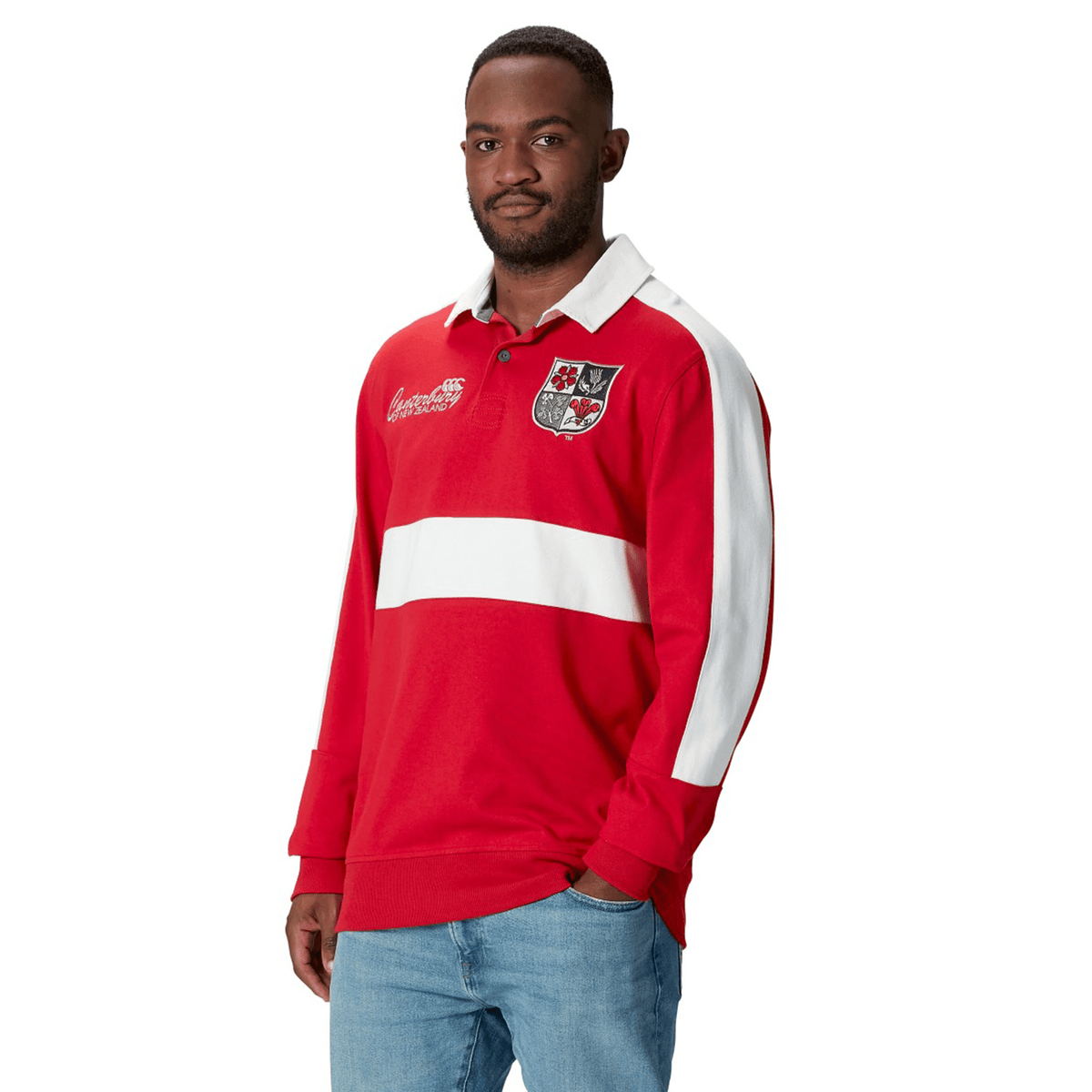 A man wearing a British &amp; Irish Lions 2025 Heritage Jersey by Canterbury, featuring white stripes, pairs it with jeans as he stands against a white background.
