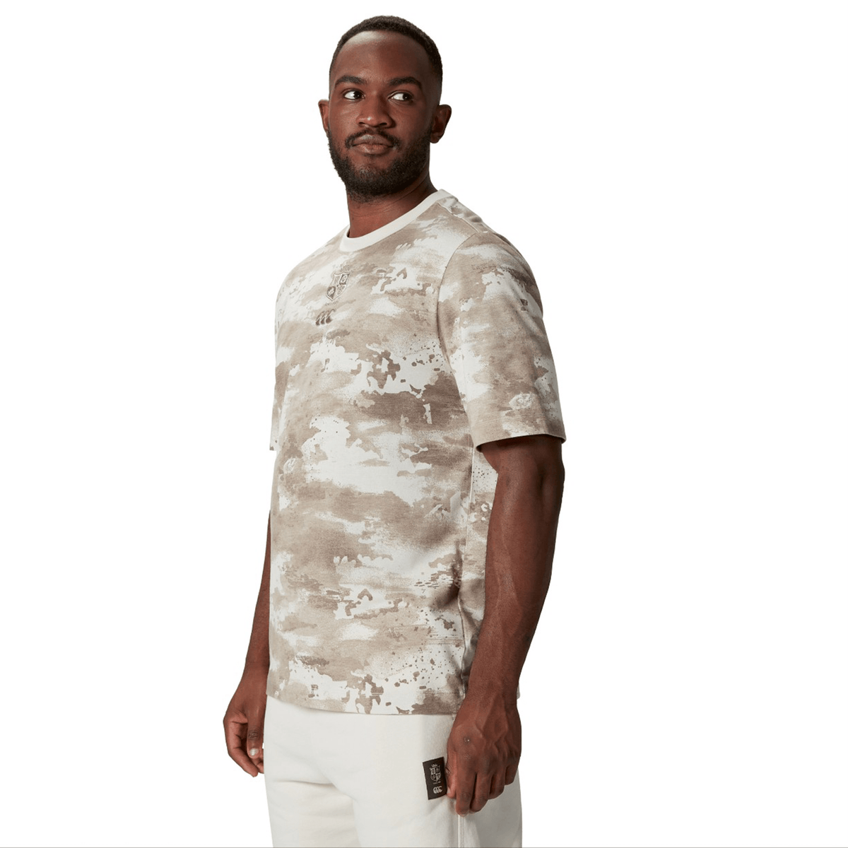 A person wearing a British &amp; Irish Lions 2025 Camo Tee by Canterbury paired with light-colored pants stands against a plain white background, exuding a subtle yet adventurous vibe.
