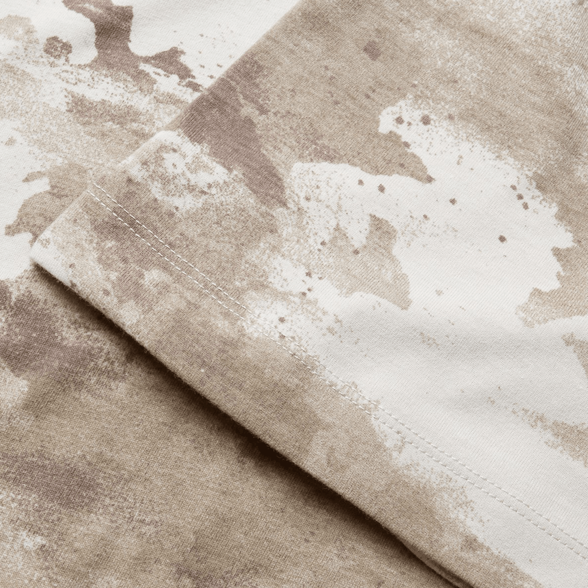 Close-up of fabric with a beige and white abstract pattern, reminiscent of the British &amp; Irish Lions 2025 Camo Tee by Canterbury, showing the edge of a seam.