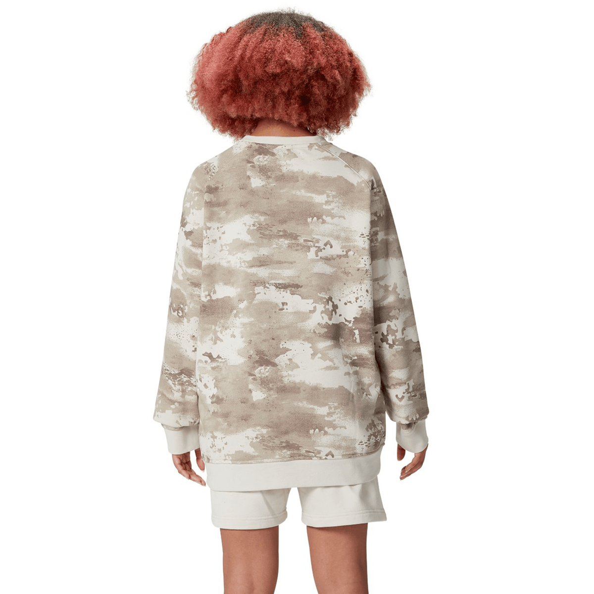 A person with curly hair is wearing the British &amp; Irish Lions 25 Camo Crew Sweatshirt by Canterbury along with white shorts, facing away from the camera.