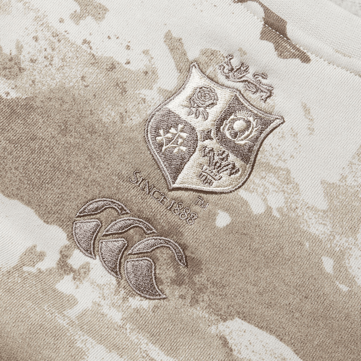 A close-up of the British &amp; Irish Lions 25 Camo Crew Sweatshirt by Canterbury showcases a beige and brown rugby jersey design. The piece proudly displays the prestigious British &amp; Irish Lions crest, accompanied by the text "Since 1888" and three stylized logos underneath, exemplifying Canterbury's timeless craftsmanship.