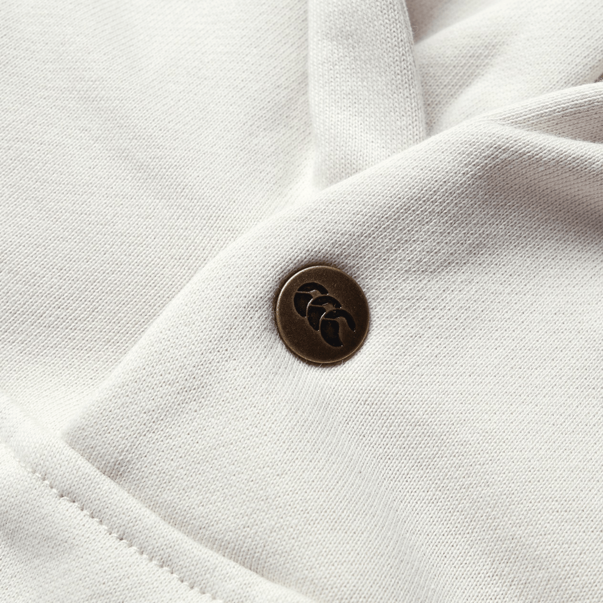 A close-up of a white fabric garment, reminiscent of the British &amp; Irish Lions 2025 Outback Fleece Hoodie by Canterbury, with a metal button featuring a leaf design.