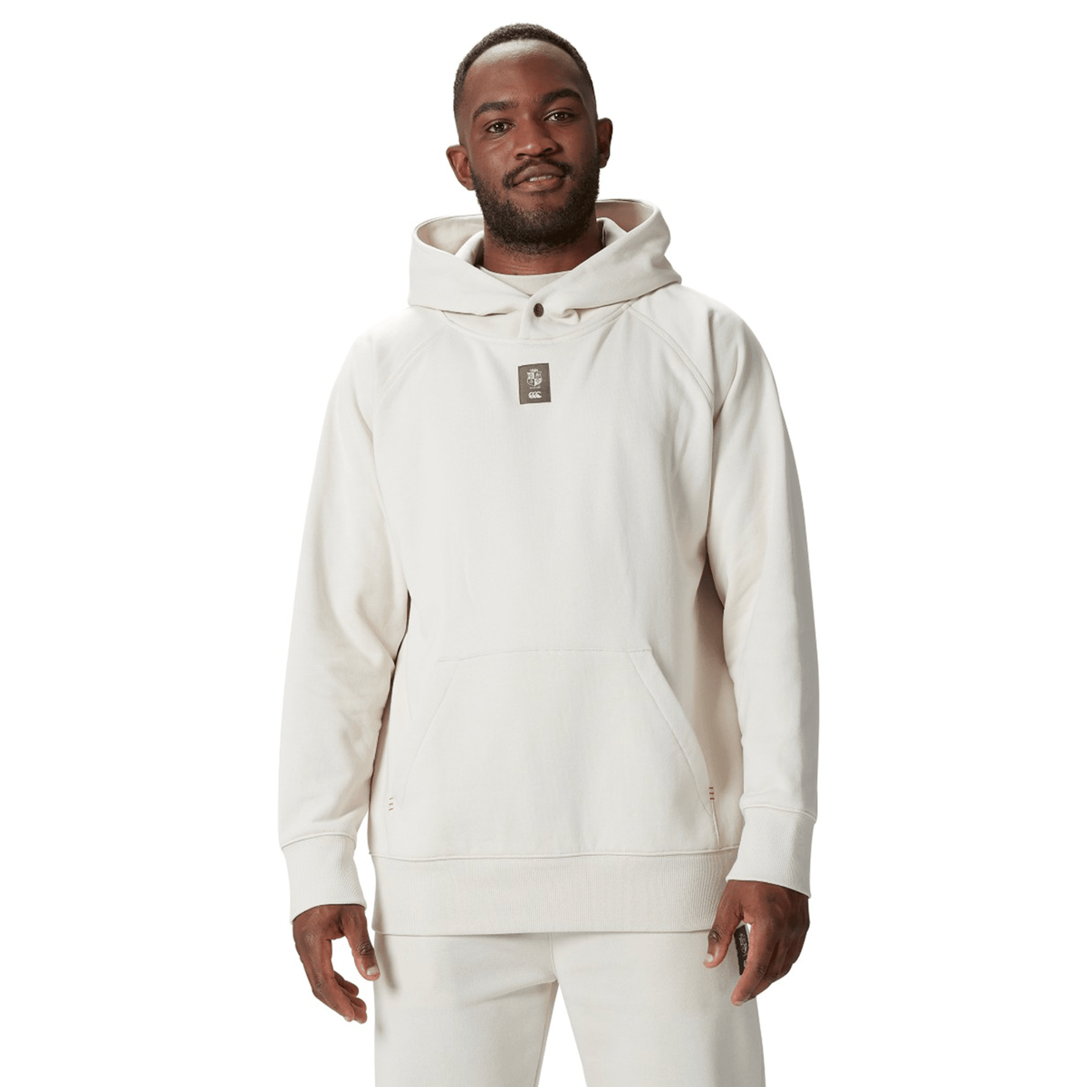 A person in a cream-colored British &amp; Irish Lions 2025 Outback Fleece Hoodie by Canterbury and matching pants stands facing forward, capturing the bold spirit of the British &amp; Irish Lions with understated style.