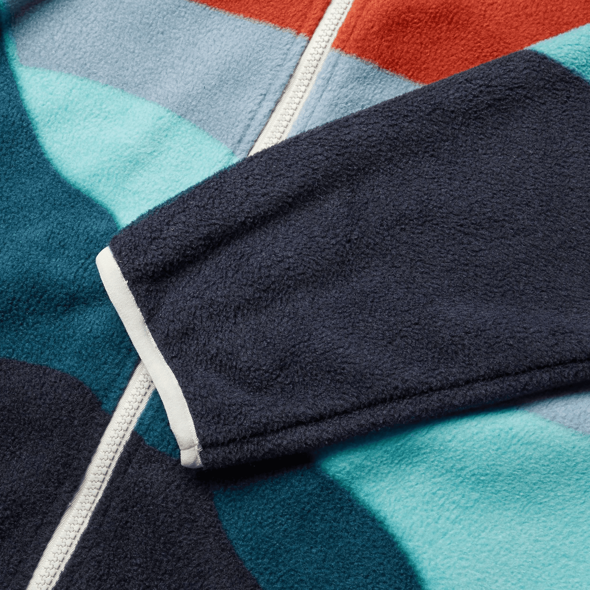 Close-up of the British &amp; Irish Lions 2025 Outback Full-Zip Fleece Jacket by Canterbury, featuring a navy sleeve and a white zipper. The fabric displays geometric patterns in shades of red, blue, and teal, echoing the iconic styles for which Canterbury is known.