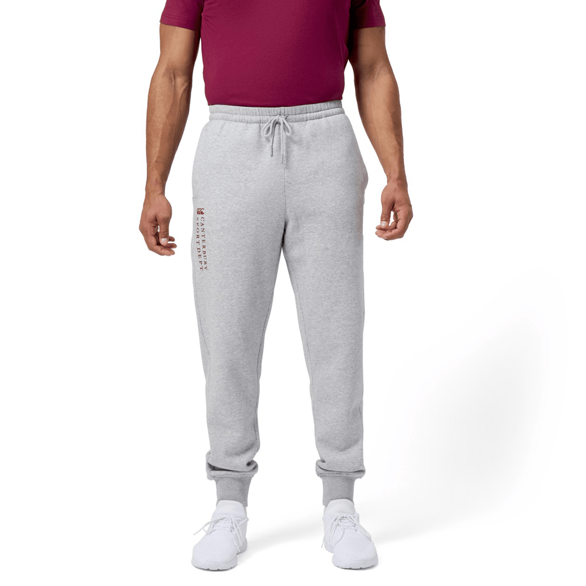 A person in Canterbury Sport Dept Track Pant with an elastic waistband, a maroon T-shirt, and white sneakers stands against a white background.