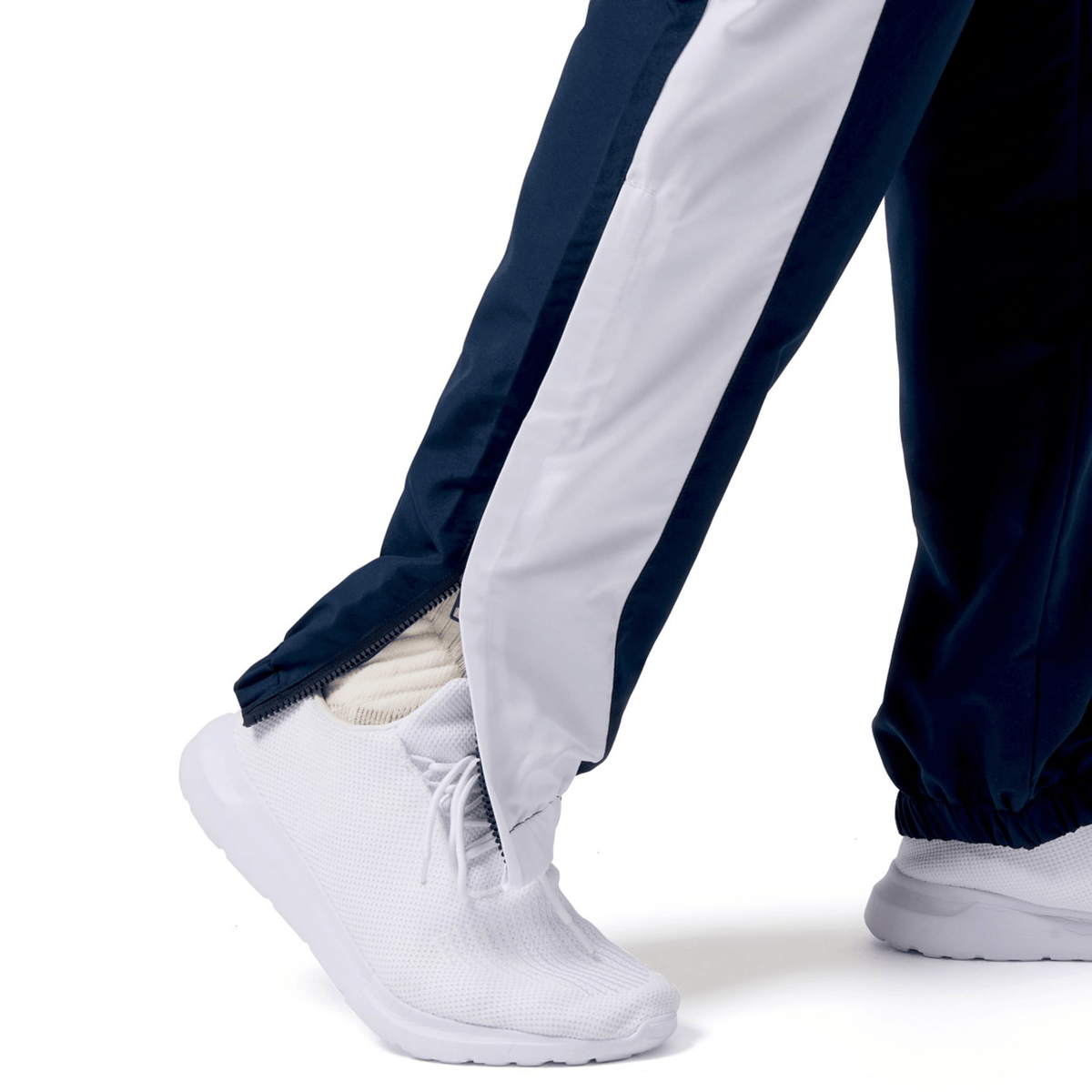 The Canterbury Harlequin Legends Trackpant in navy and white is a rugby fan's wardrobe staple, pairing effortlessly with sleek white sneakers. It features a partially open zippered hem over the shoe for a stylish flair.