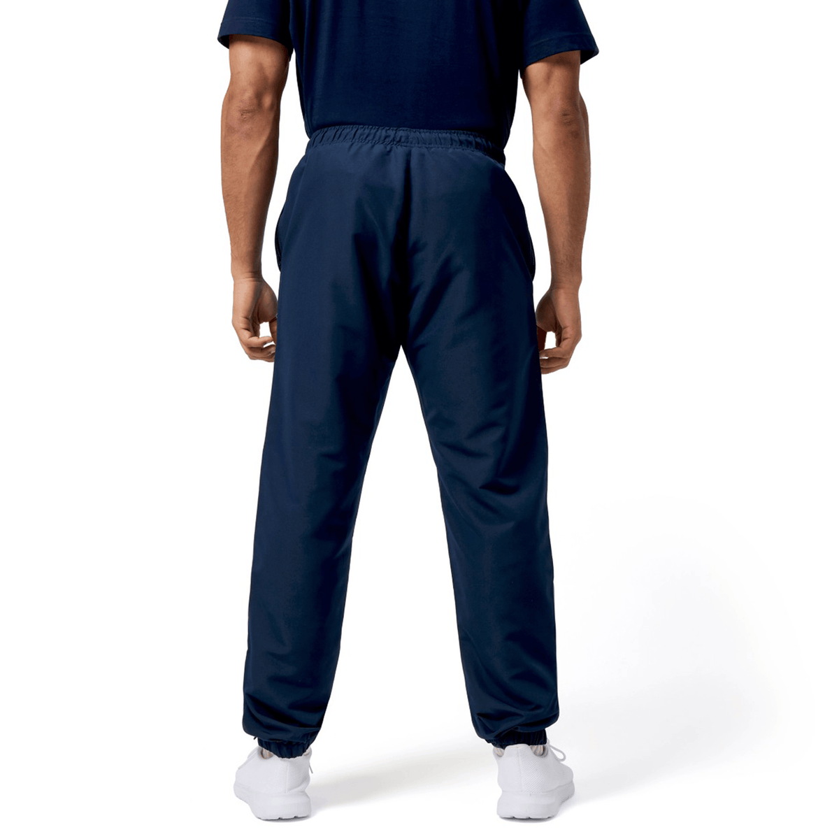 A person in Canterbury Harlequin Legends Trackpant and matching navy blue shirt stands with their back to the camera, embodying Canterbury's classic style. White sneakers complete the look against a white backdrop—ideal for a rugby enthusiast's wardrobe.