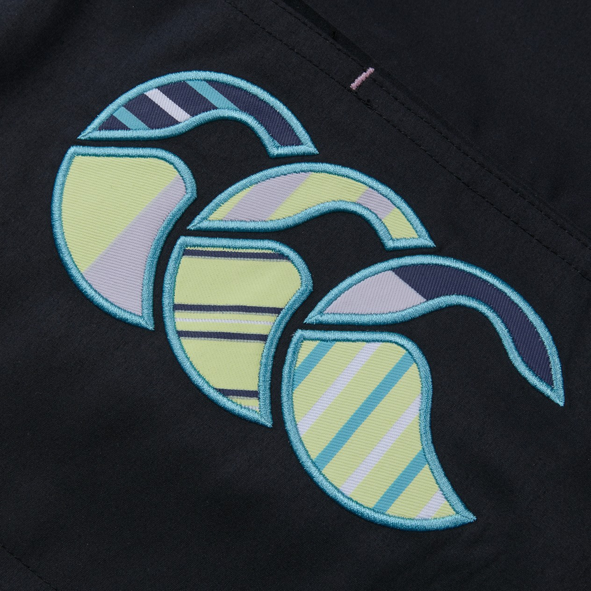 The Women&#39;s Canterbury Uglies 5&quot; Tactic Short by Canterbury features embroidery of three overlapping stylized waves with striped patterns in blue, green, and purple tones on a dark polyester fabric background.