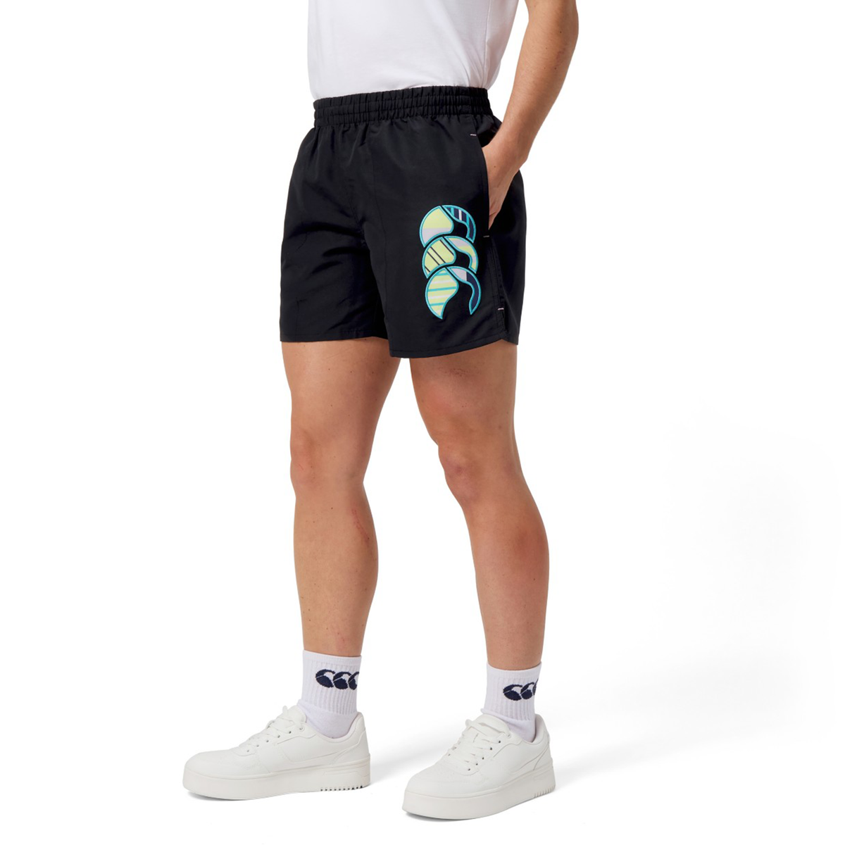 A person in a white shirt and sneakers wears Canterbury Uglies Women&#39;s 5&quot; Tactic Shorts, showcasing a vibrant green and blue spiral design. Made from durable polyester fabric, they add flair to any casual look.