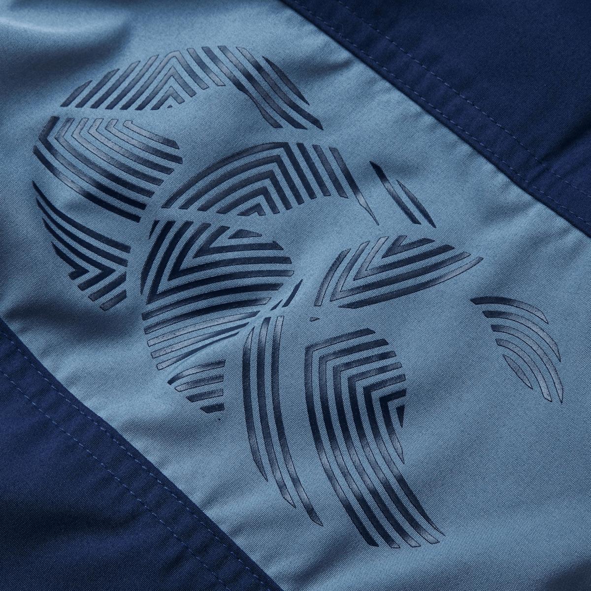 Close-up of a dark blue fabric with a geometric pattern of overlapping lines forming circular shapes, similar to the Canterbury Fundamental 5" Panel Tactic Short. This design stands out against the lighter blue background ideal for moisture-wicking shorts by Canterbury.