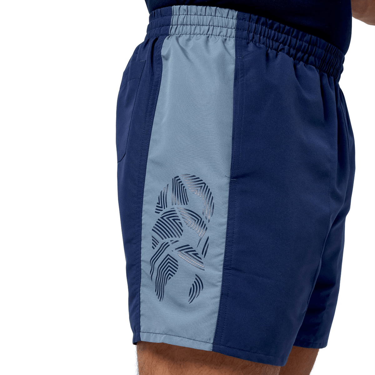 A person wears blue and gray Canterbury Fundamental 5" Panel Tactic Shorts, showcasing a geometric pattern on the side. Designed for comfort during intense workouts, these shorts dry quickly.