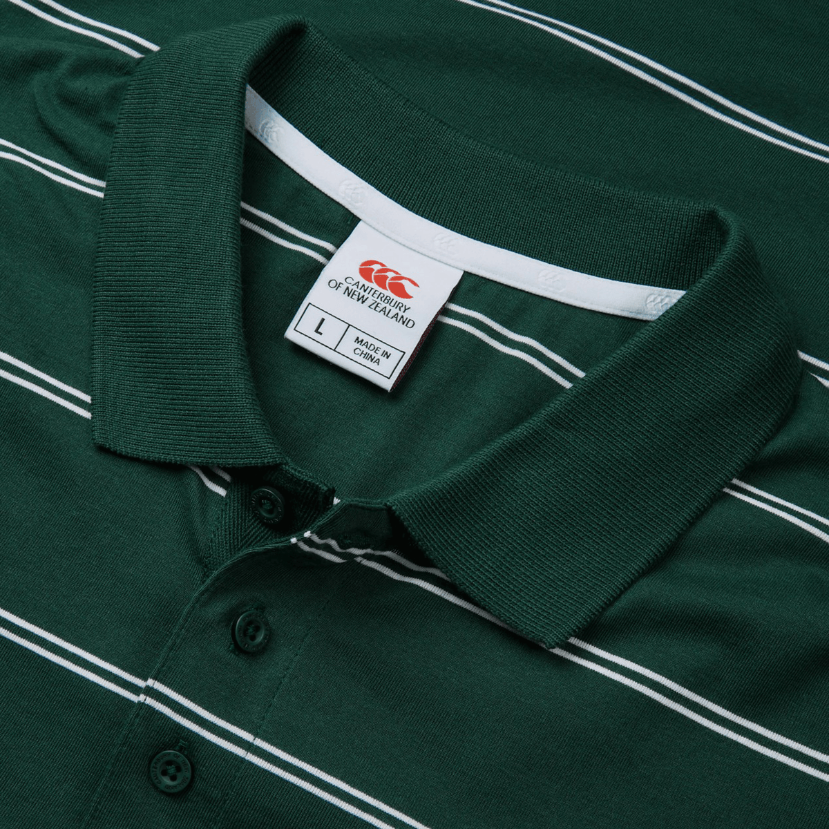 The Canterbury Fundamental Yarn-Dye Stripe Polo is green with white horizontal stripes and a collar, featuring a size "L" tag and the Canterbury brand logo.