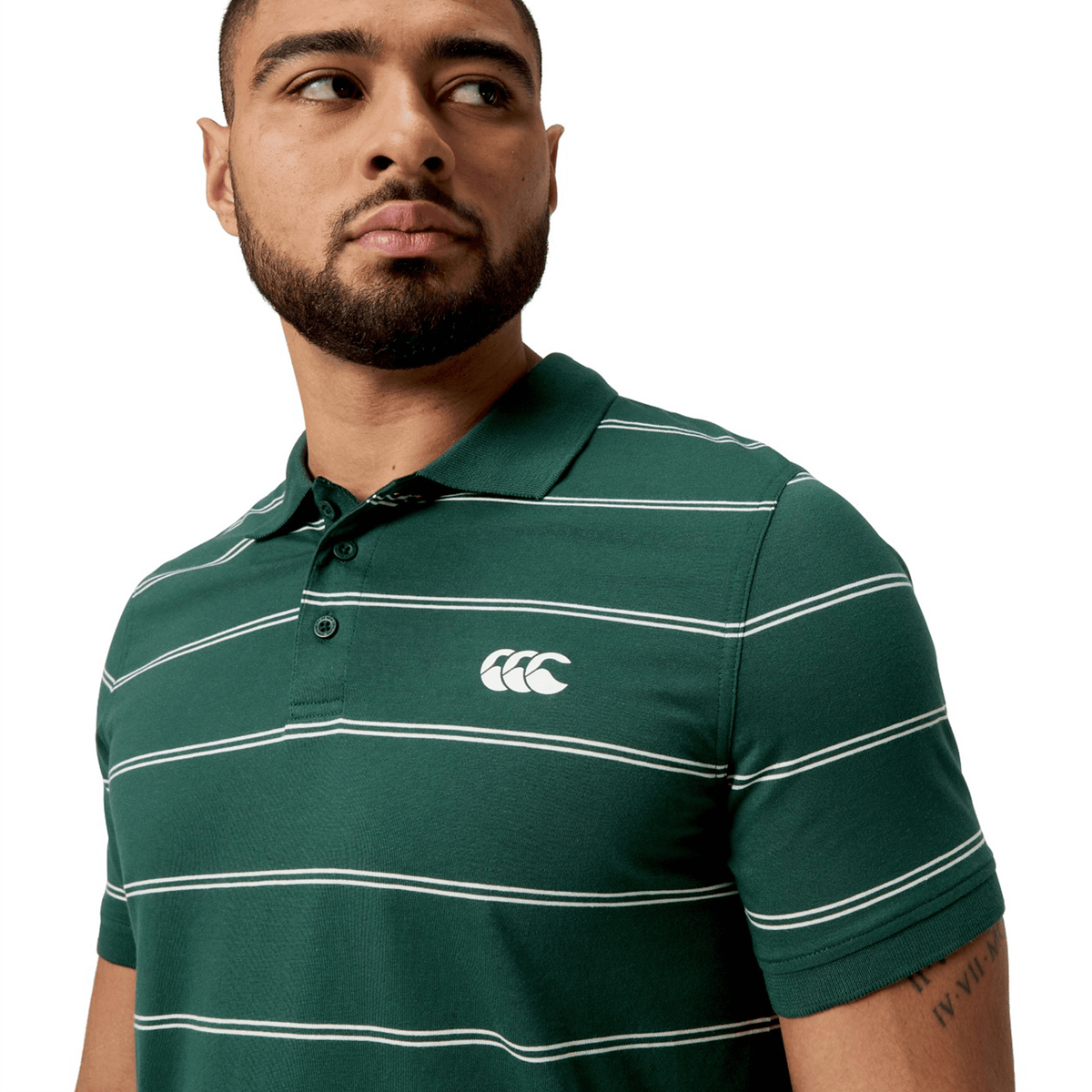 A person wearing the Canterbury Fundamental Yarn-Dye Stripe Polo with yarn-dye stripes and a chest logo gazes to the side.