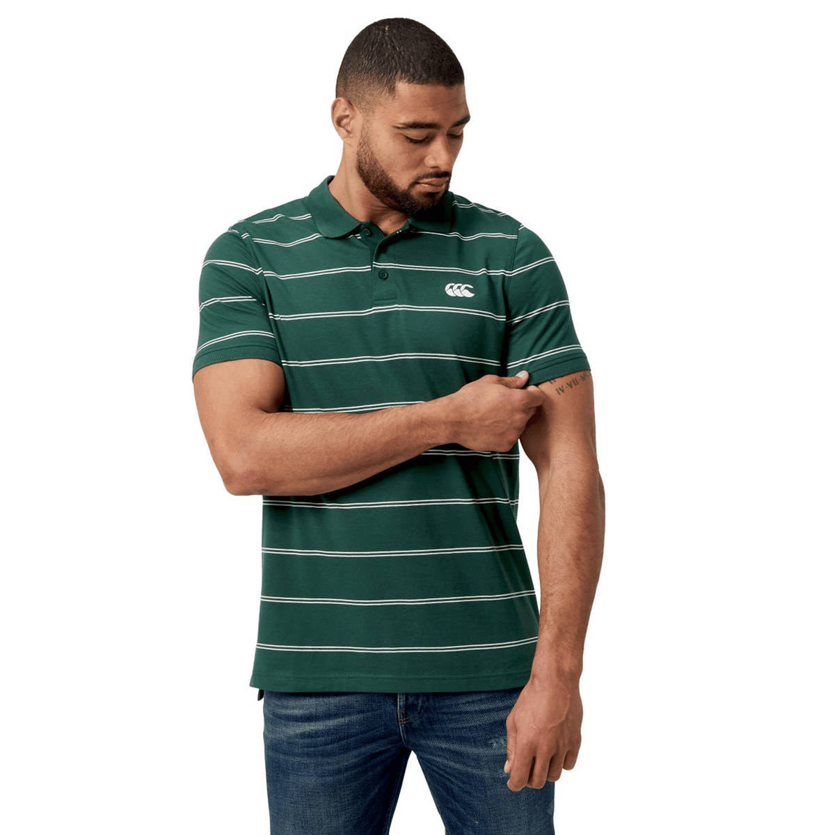 A man in a Canterbury Fundamental Yarn-Dye Stripe Polo with jeans examines his arm.
