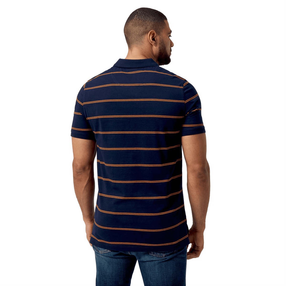 A man stands facing away, dressed in a Canterbury Fundamental Yarn-Dye Stripe Polo featuring navy blue and bold orange stripes, with classic jeans.
