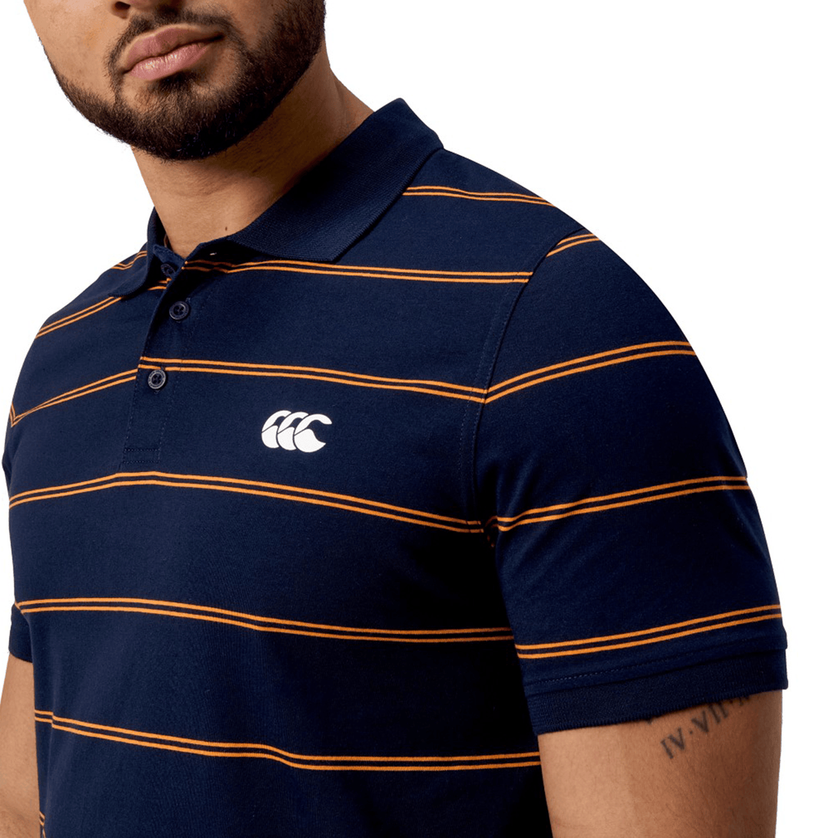 A man stands against a white background, wearing the Canterbury Fundamental Yarn-Dye Stripe Polo with bold navy and orange stripes and a chest logo.