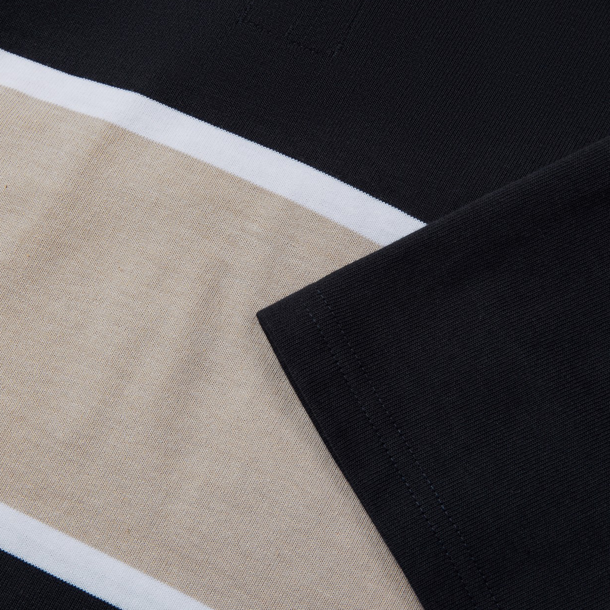 Close-up of a Canterbury Yarn Dye Rugby Jersey featuring black and beige horizontal stripes with a white stripe in between, showcasing its classic Polo Shirt design. The short sleeve highlights the refined craftsmanship typical of the Canterbury brand.