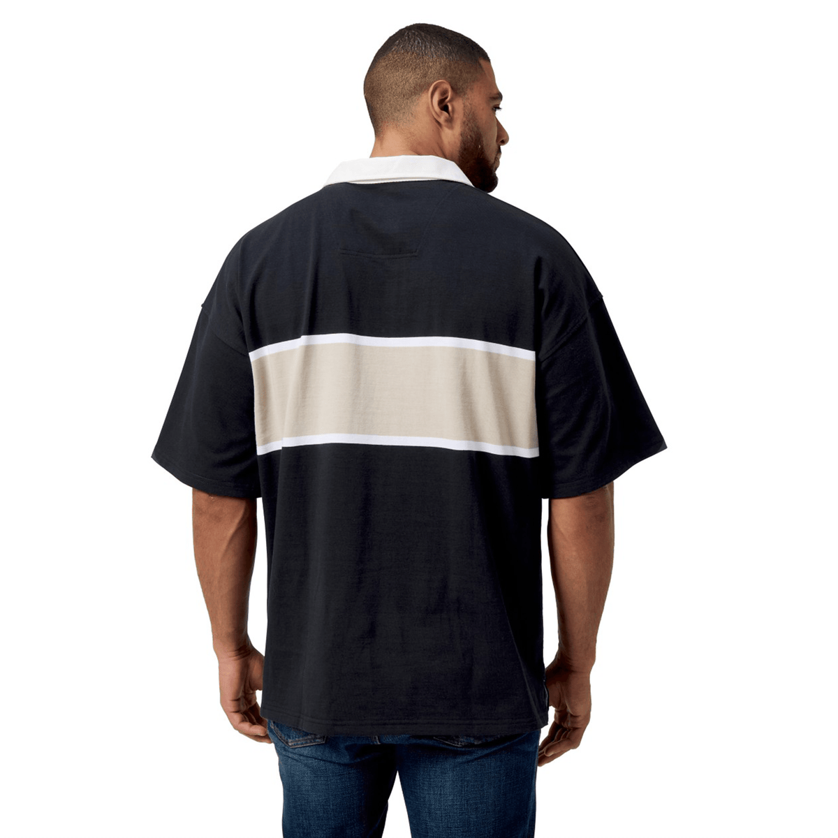 A man stands with his back to the camera, dressed in a Canterbury Yarn Dye Short Sleeve Rugby Jersey, which features black fabric adorned with white and beige horizontal stripes.