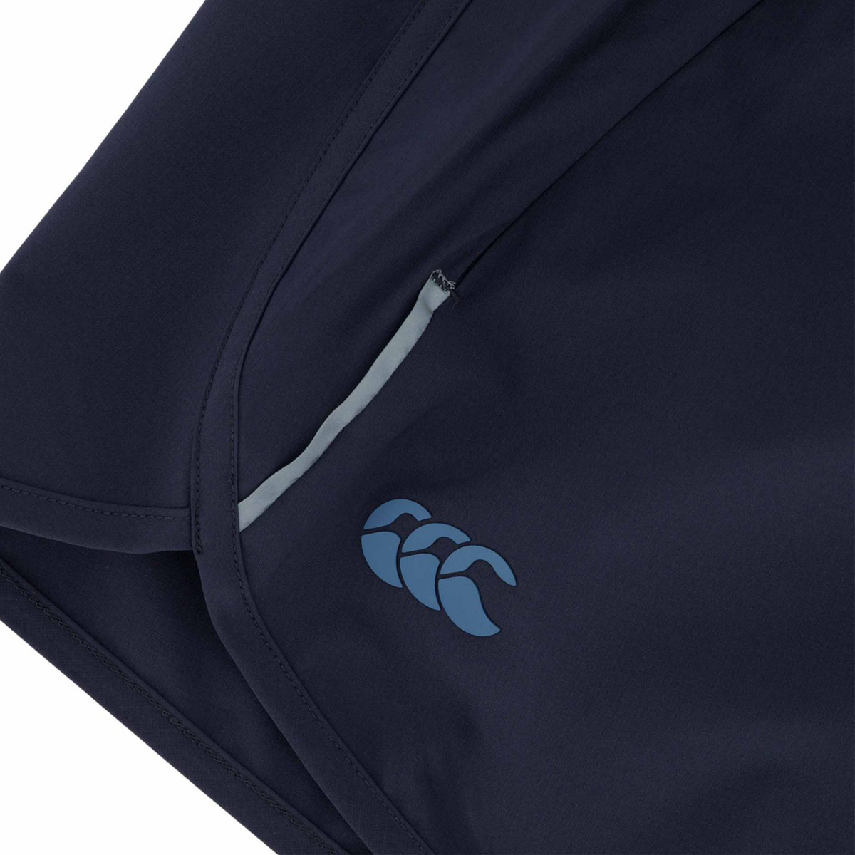 Close-up of the Canterbury Women&#39;s Tempo+ 5&quot; Training Shorts in dark navy blue, featuring a small logo with three light blue shapes near the pocket, made from a flexible and durable polyester-elastane blend.