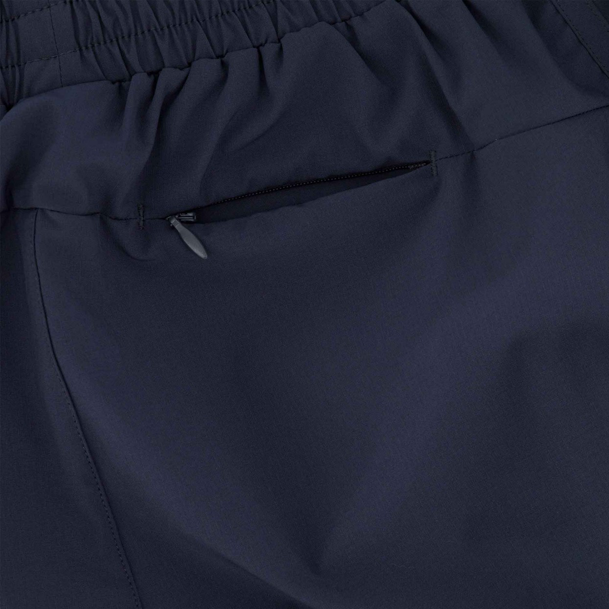Close-up of the Women&#39;s Canterbury Tempo+ 5&quot; Training Short in navy, featuring a visible elastic waistband and a horizontal zippered pocket. The polyester-elastane blend enhances comfort, while subtle reflective piping adds style and safety.