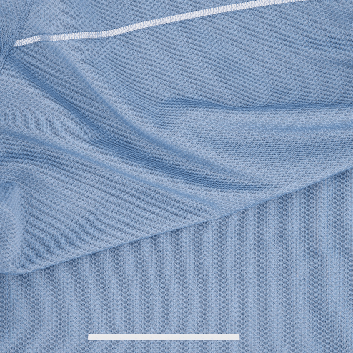 Close-up of the Canterbury Tempo+ Training Tee in light blue textured, moisture-wicking fabric, showcasing a thin white line with reflective detailing running diagonally across the top.