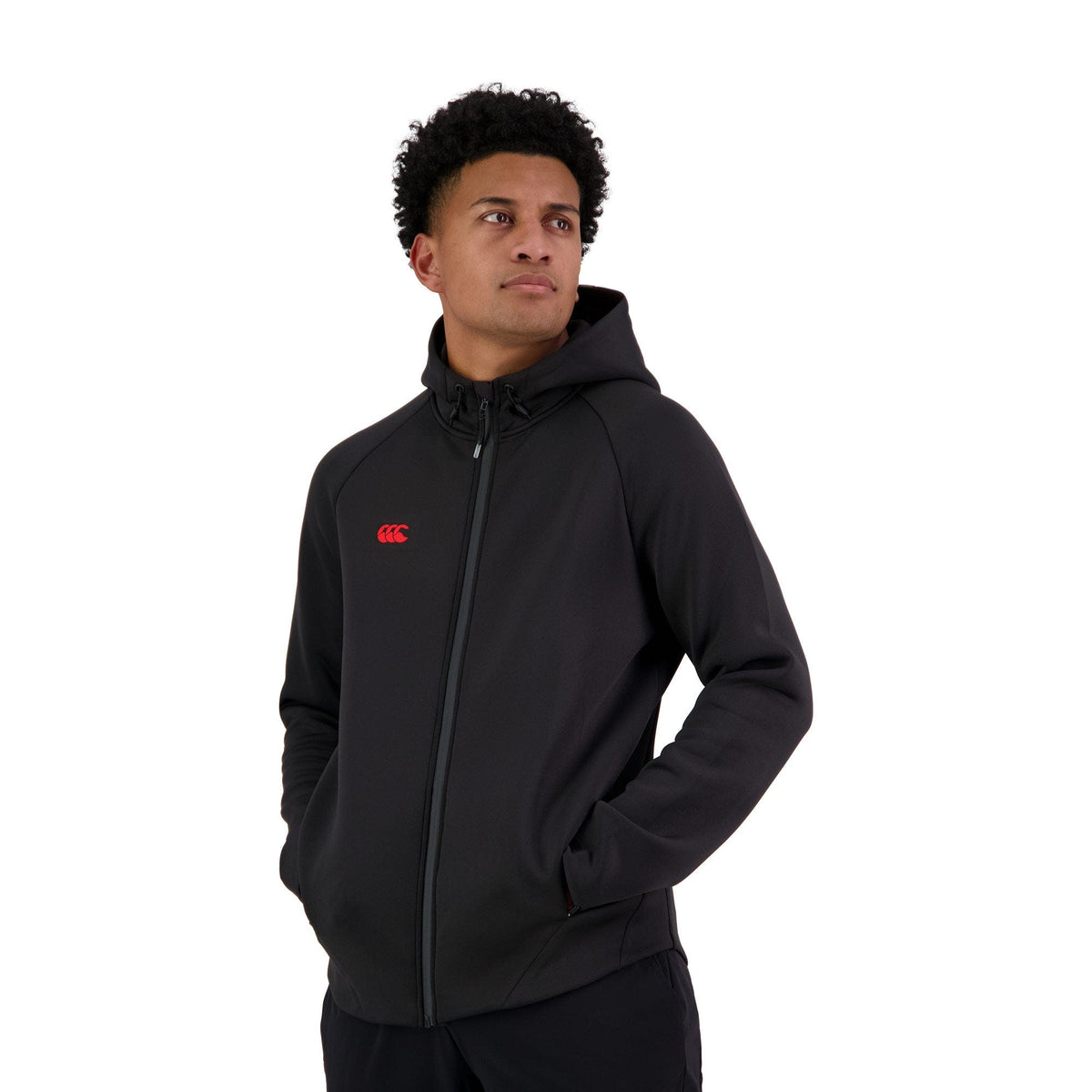 Wearing the Canterbury Everest Full-Zip Hoodie, complete with invisible zip pockets and a chest red logo, a person stands confidently against a stark white background, hands tucked away and looking slightly to the side, embodying the ideal training companion.