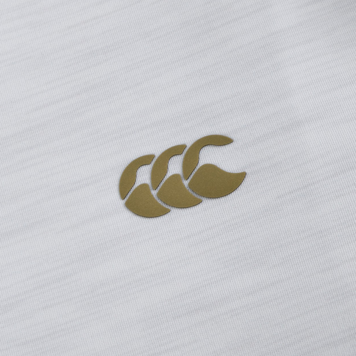 Close-up of the Everest Training Full-Zip Hoodie by Canterbury, showcasing a white fabric with Canterbury’s gold CCC logo—three stylized overlapping C shapes—ideal for lightweight athletic wear.